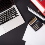 Business professional reviewing financial documents with a laptop and calculator in an office environment.